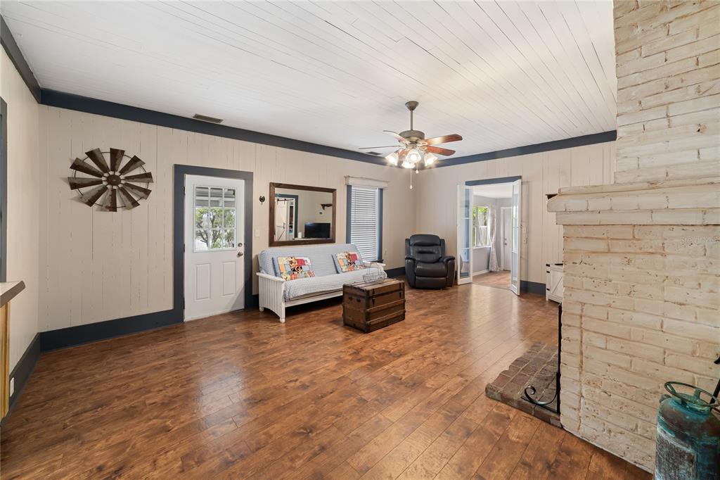 A living room features wood-look flooring, a white brick fireplace, and a ceiling fan — 1905 MYRTLE LAKE AVENUE, FRUITLAND PARK, FL