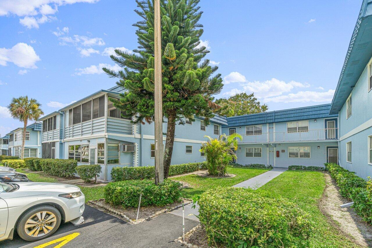 A two-story blue apartment building with a central courtyard, landscaping, and a parking lot — 260 Brittany F, Delray Beach FL 33446, DELRAY BEACH, FL