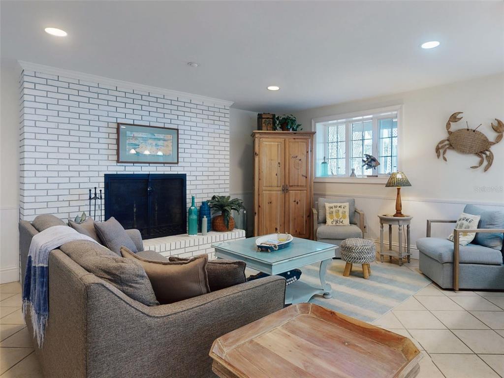 A living room features a white brick fireplace, gray sofa, armchairs, and a wooden cabinet — 1913 HILL STREET UNIT 1, NEW SMYRNA BEACH, FL