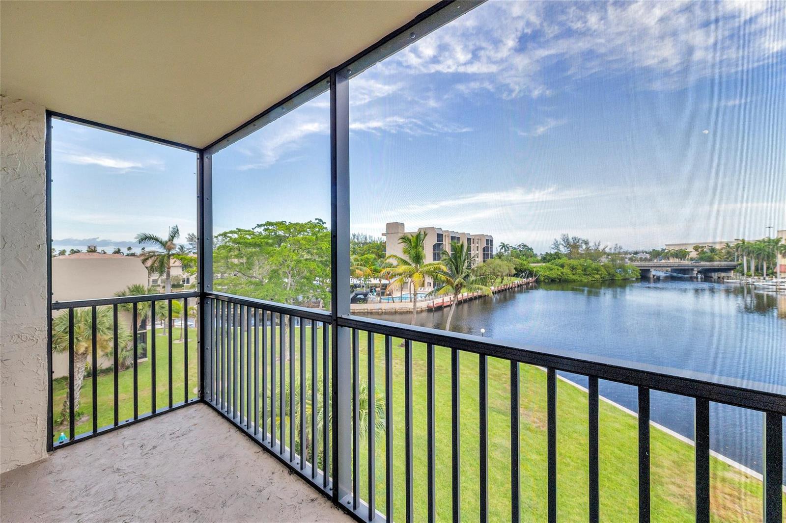 A screened-in balcony overlooks a grassy lawn, a canal, and distant buildings under a blue sky — 7 Royal Palm Way, Boca Raton FL 33432, BOCA RATON, FL