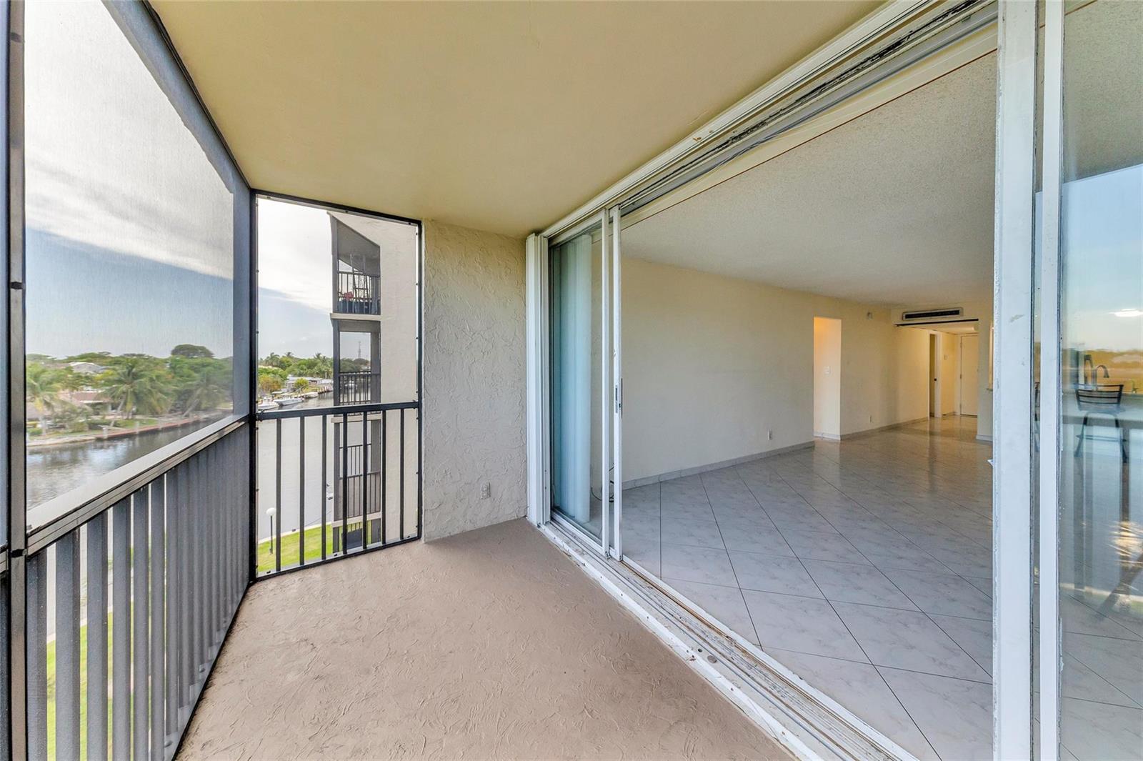 A balcony with a screen enclosure overlooks a canal next to an empty tiled room — 7 Royal Palm Way, Boca Raton FL 33432, BOCA RATON, FL