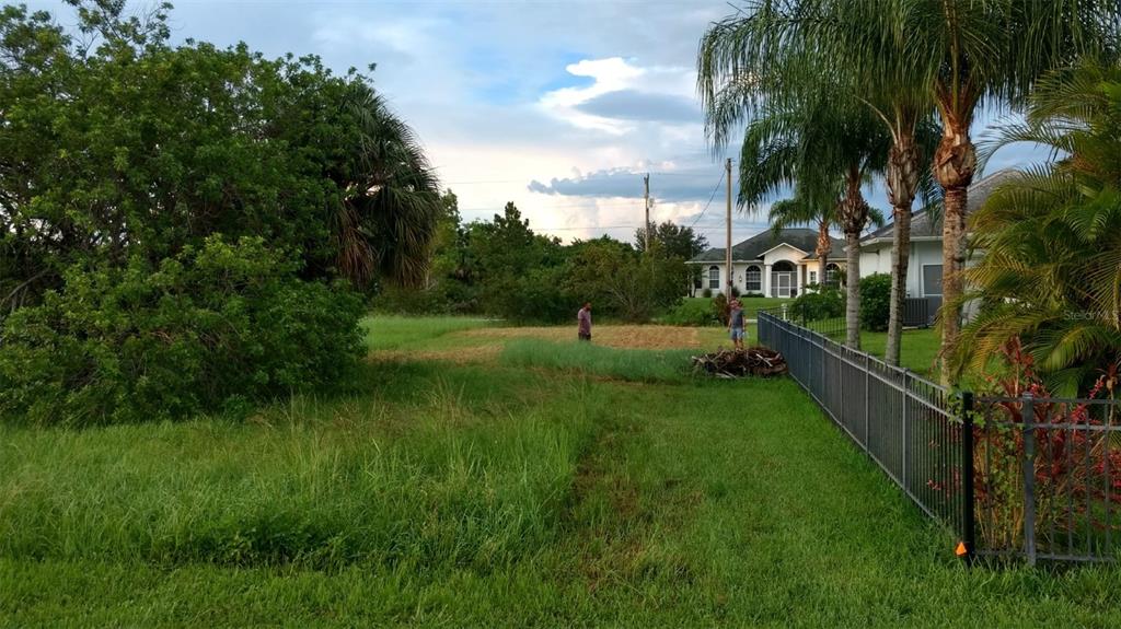 A grassy lot with two people standing in a cleared area near a metal fence — 670 MIRROR LAKES COURT, LEHIGH ACRES, FL