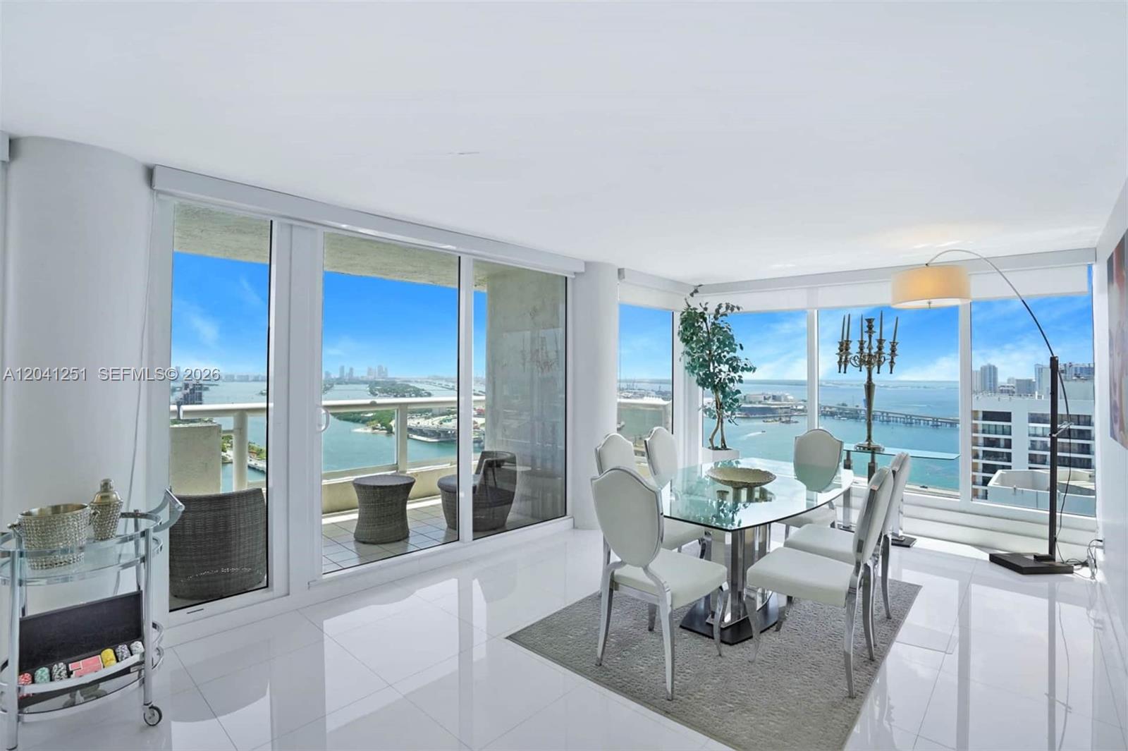 A dining room with a glass table, white chairs, and floor-to-ceiling windows overlooking water — 1717 N Bayshore Dr # 3931, Miami FL 33132, MIAMI, FL
