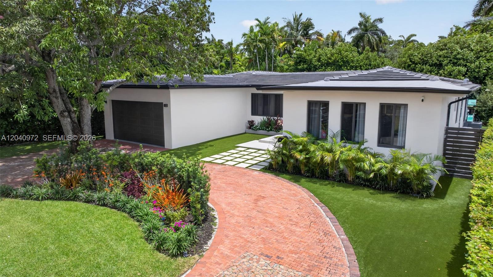 A white single-story house with a brick driveway, artificial turf, and a dark garage door — 645 NE 53rd St, Miami FL 33137, MIAMI, FL