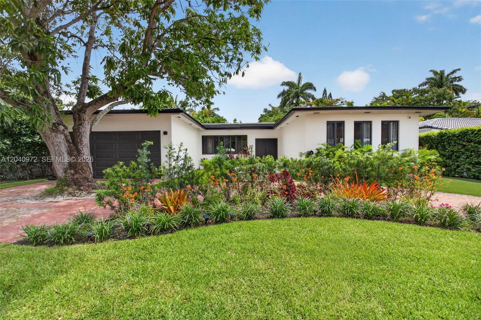A single-story white house with a dark garage and lush landscaping sits behind a lawn — 645 NE 53rd St, Miami FL 33137, MIAMI, FL