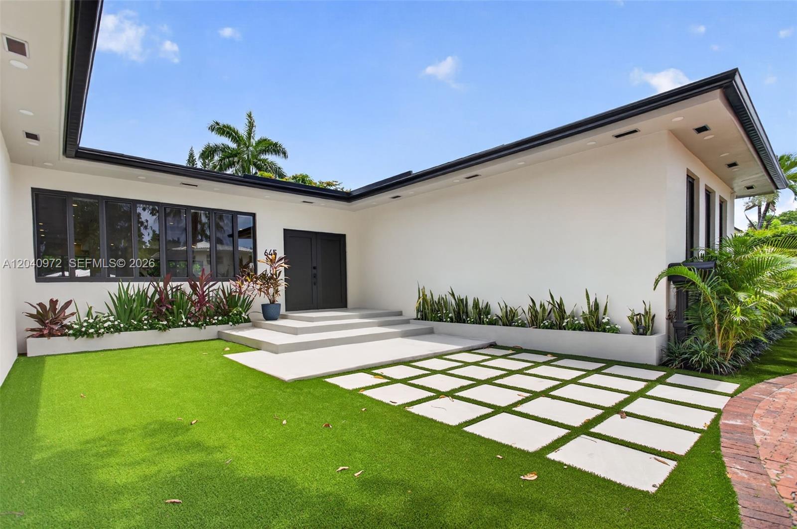 A modern house exterior features a white facade, dark-framed windows, and a paved entryway — 645 NE 53rd St, Miami FL 33137, MIAMI, FL