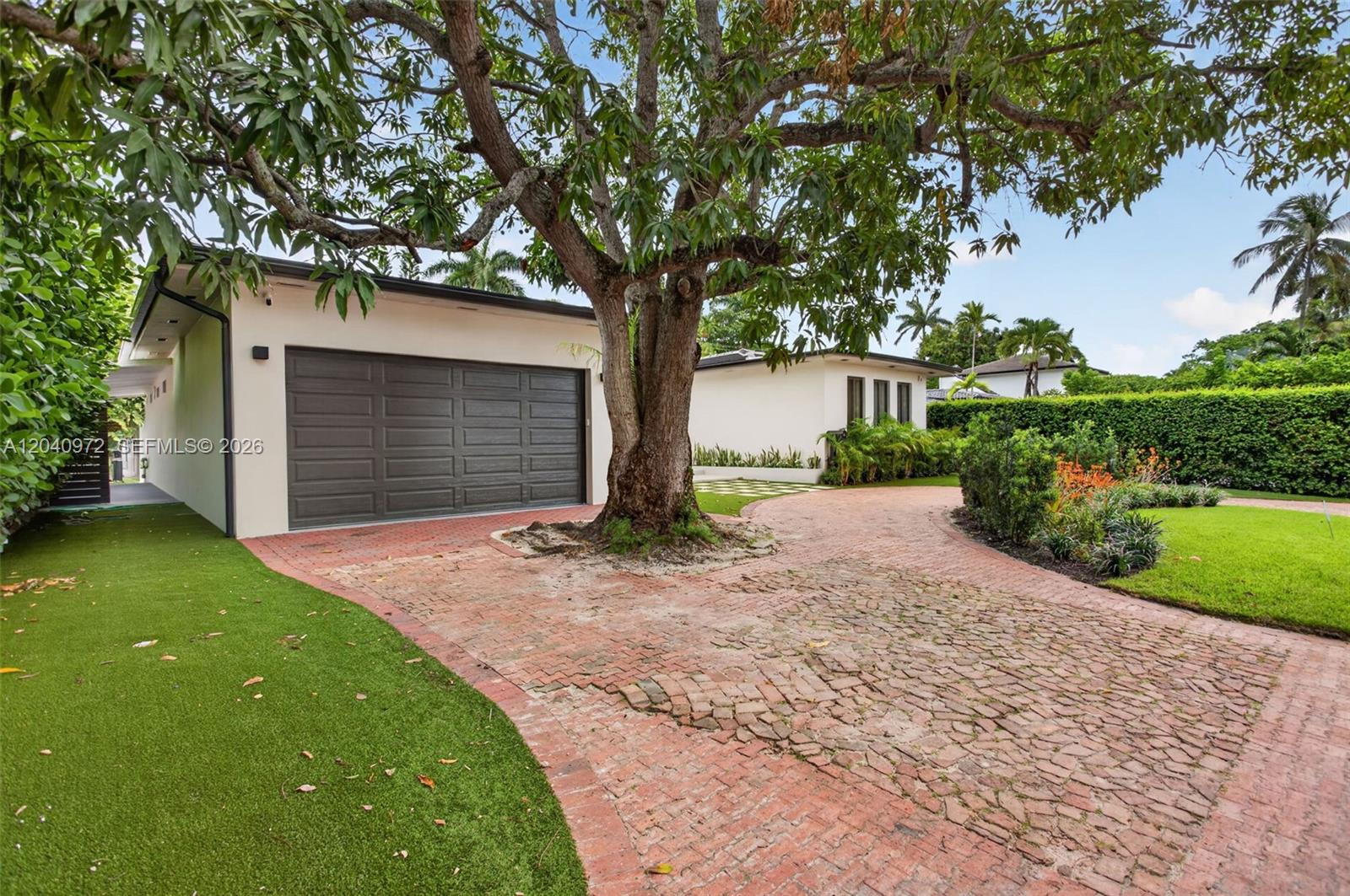 A large tree stands in the center of a brick driveway leading to a garage — 645 NE 53rd St, Miami FL 33137, MIAMI, FL