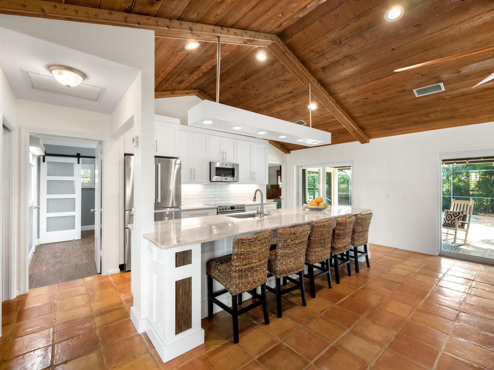 A kitchen with white cabinets, a large island with wicker stools, and a wood-paneled ceiling — 52 Birch Place, Tequesta FL 33469, TEQUESTA, FL