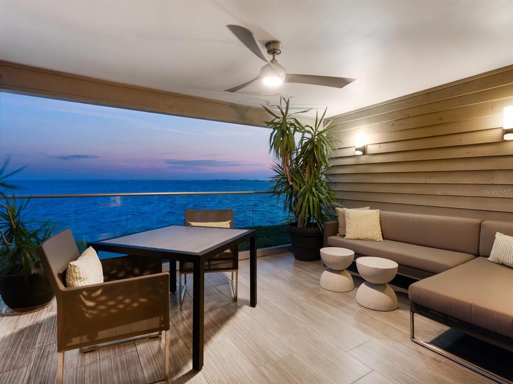 A covered balcony features a dining set, sectional sofa, ceiling fan, and ocean views — 26 TIDY ISLAND BOULEVARD, BRADENTON, FL