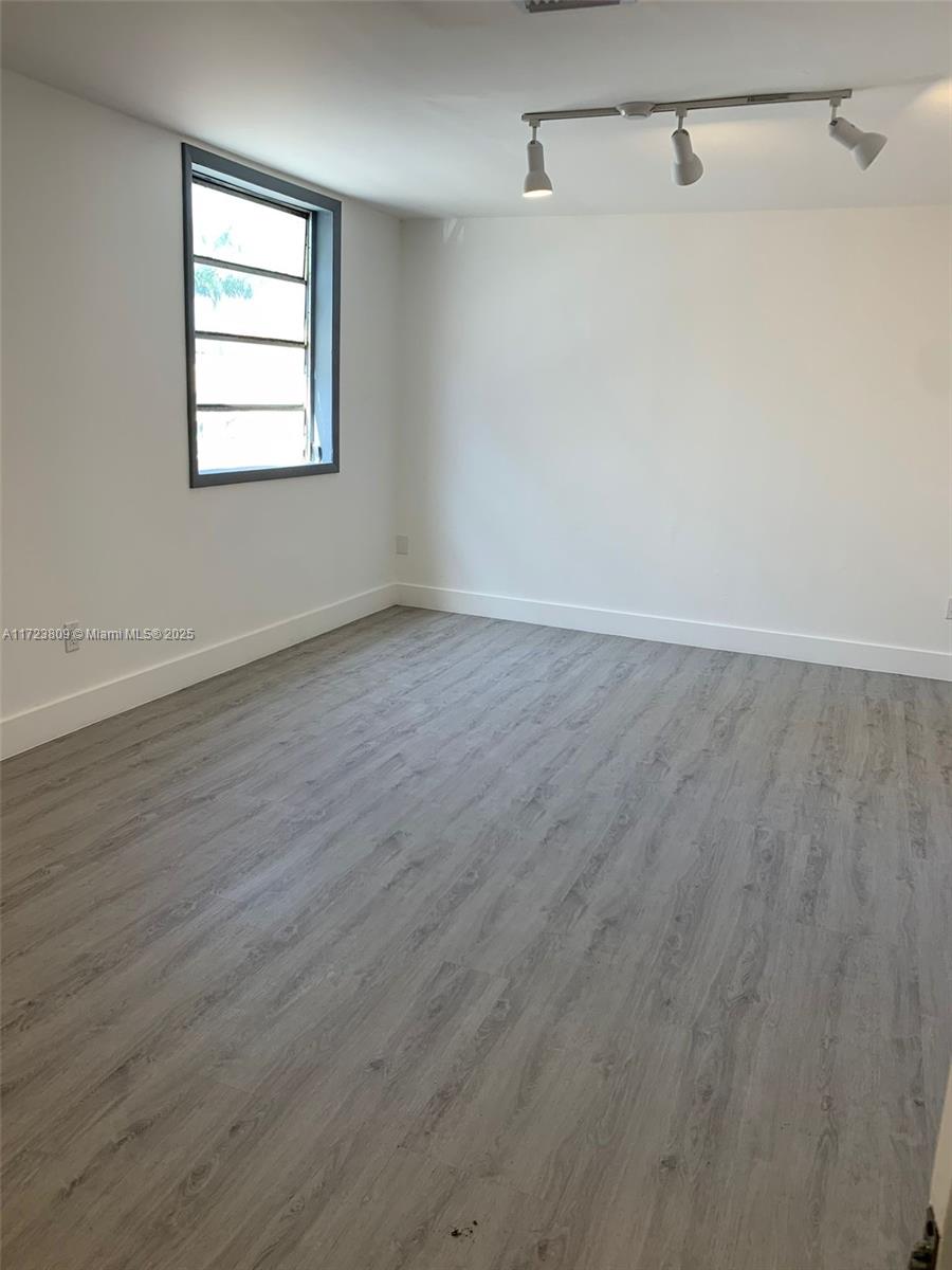 An empty room features white walls, gray wood-look flooring, and a track lighting fixture — 638 NW 62nd St, Miami FL 33150, MIAMI, FL