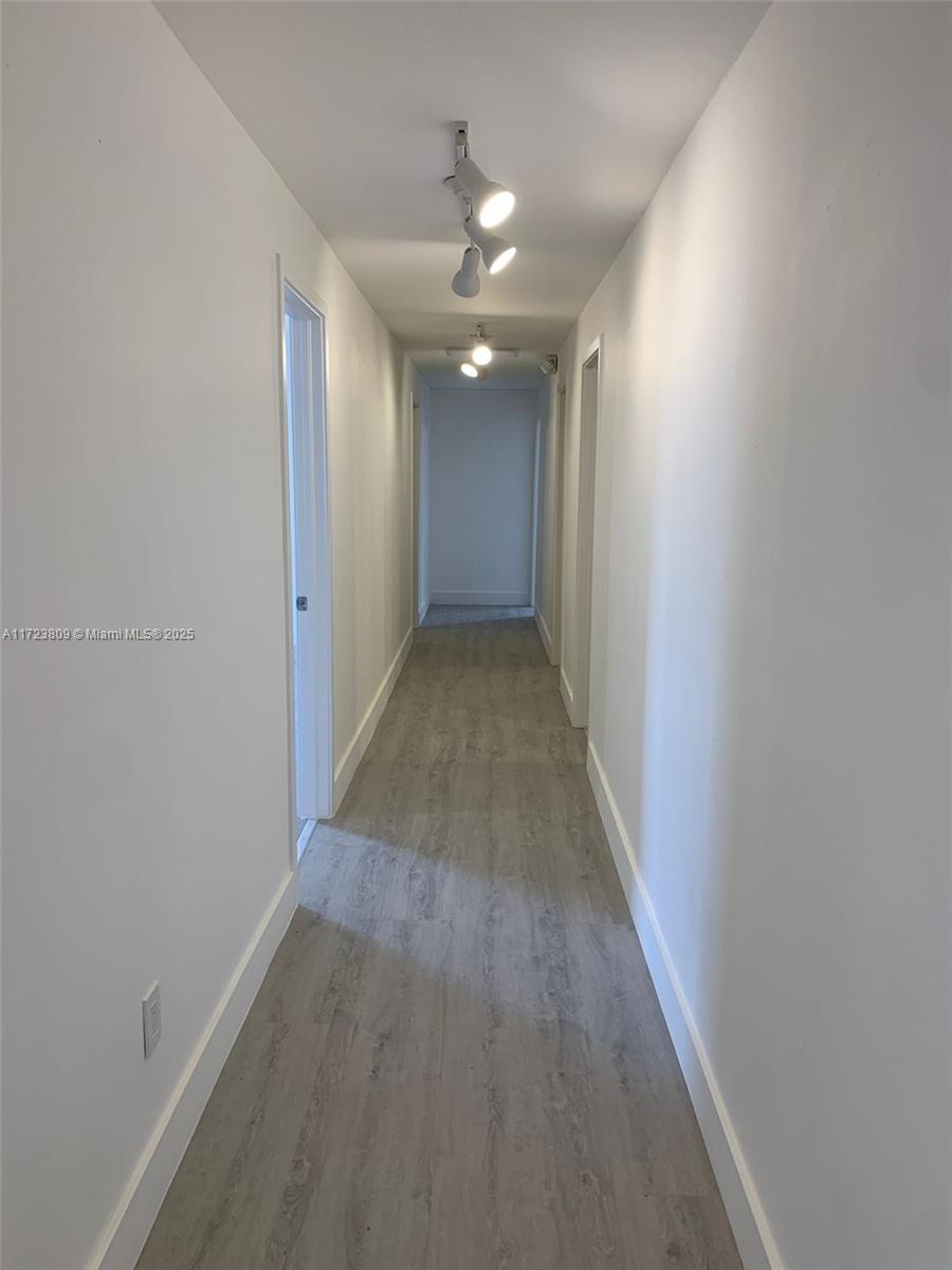A long, narrow hallway features light gray wood-look flooring, white walls, and track lighting — 638 NW 62nd St, Miami FL 33150, MIAMI, FL