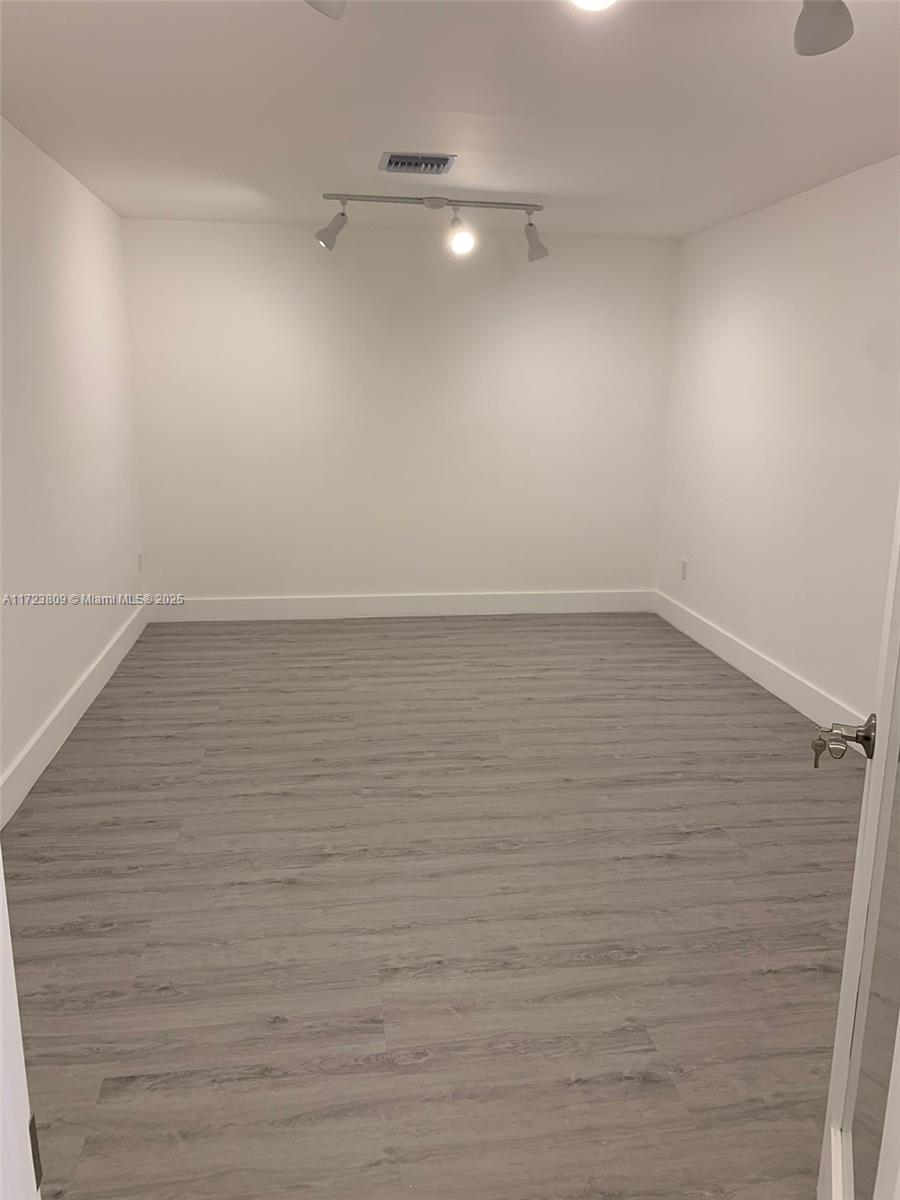An empty room features white walls, gray wood-look flooring, and a ceiling-mounted track lighting fixture — 638 NW 62nd St, Miami FL 33150, MIAMI, FL