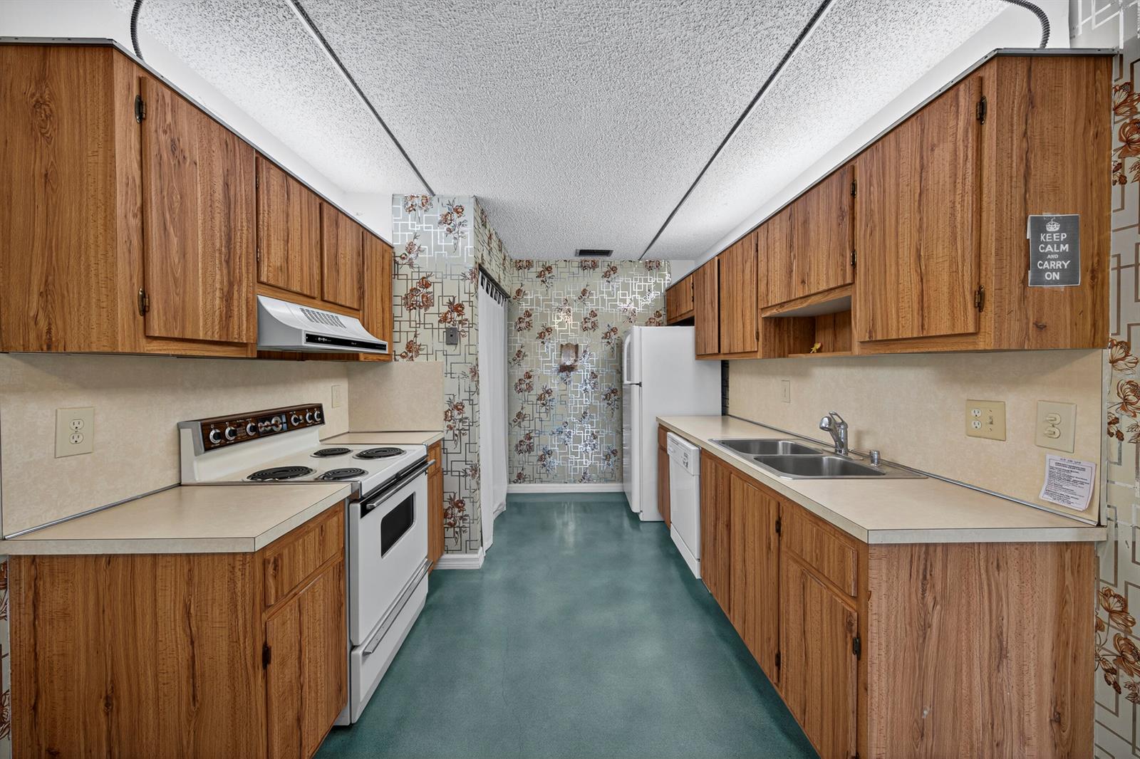 A galley kitchen features wood cabinets, laminate countertops, floral wallpaper, and a teal floor — 14236 Campanelli Drive, Delray Beach FL 33484, DELRAY BEACH, FL