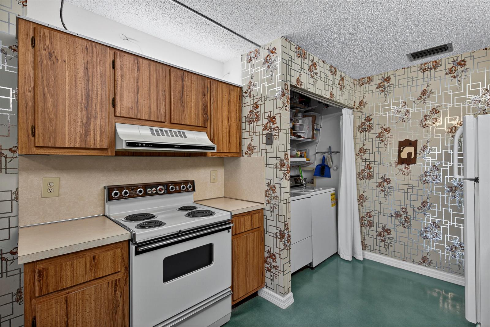 A kitchen features wood cabinets, a white electric stove, and patterned wallpaper with a laundry closet — 14236 Campanelli Drive, Delray Beach FL 33484, DELRAY BEACH, FL