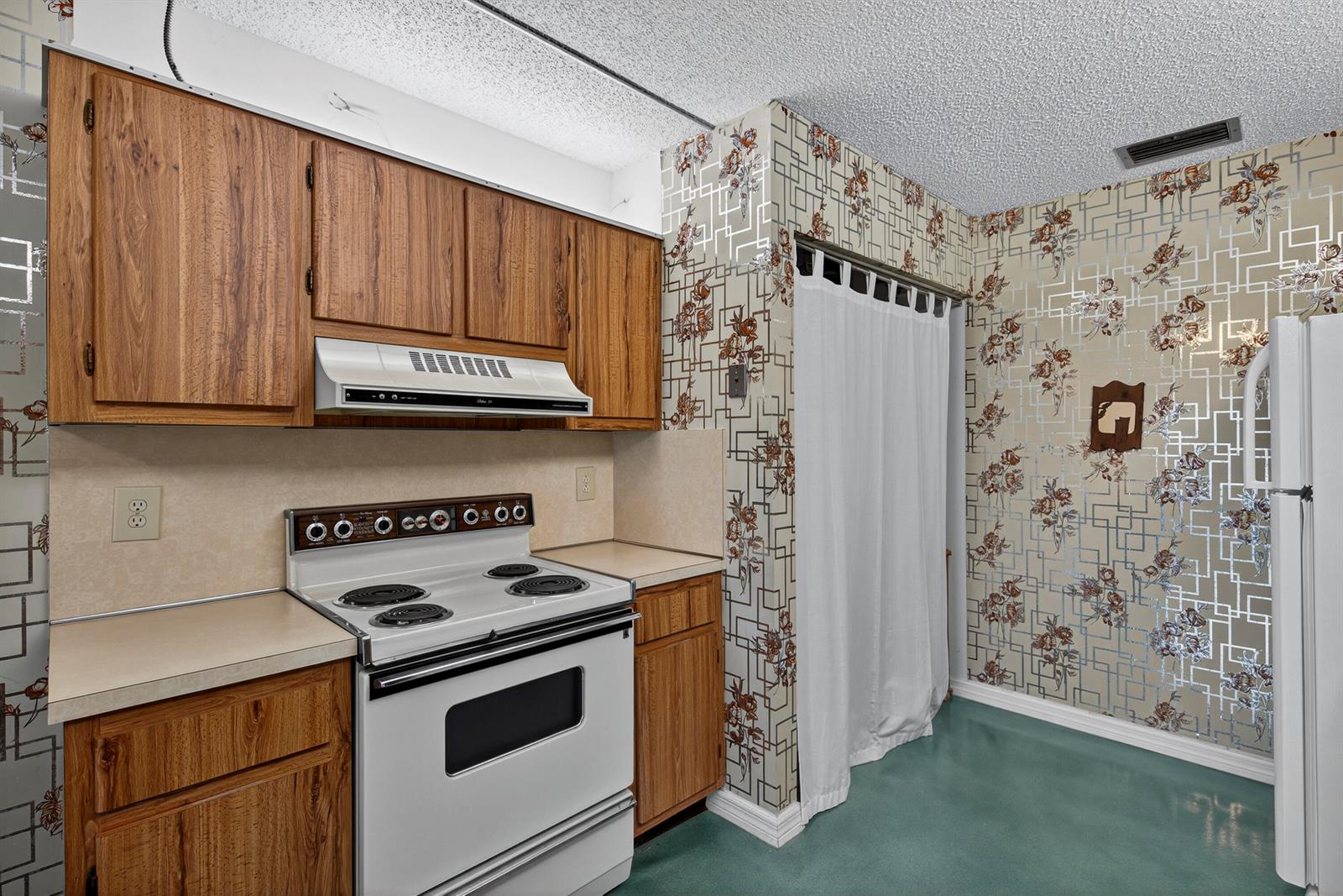 A kitchen features wood cabinets, a white stove, and patterned wallpaper with a floral design — 14236 Campanelli Drive, Delray Beach FL 33484, DELRAY BEACH, FL