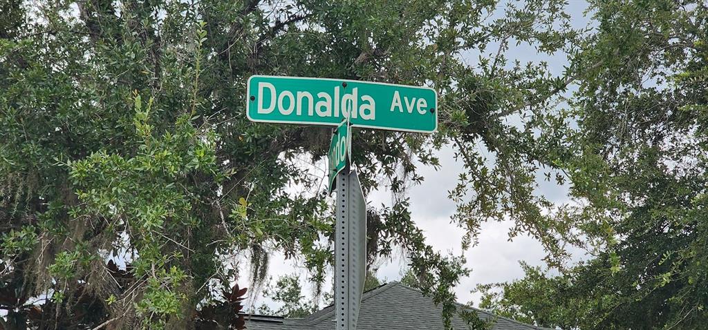 A green street sign for Donalda Ave is mounted on a pole against leafy trees — 22436 DONALDA AVENUE, PORT CHARLOTTE, FL