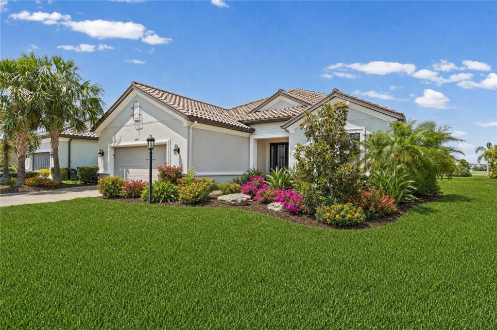 A single-story house with a tiled roof, garage, and landscaped front yard under blue skies — 14817 MONTELLO WAY, BRADENTON, FL