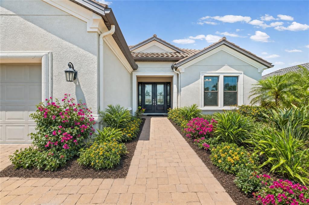 A paved walkway leads to the front entrance of a house with light-colored stucco walls — 14817 MONTELLO WAY, BRADENTON, FL