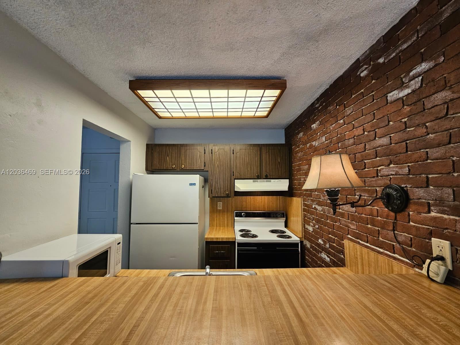 A kitchen features wood-grain countertops, dark wood cabinets, a white stove, and a brick wall — 520 NE 38th St # 12, Miami FL 33137, MIAMI, FL
