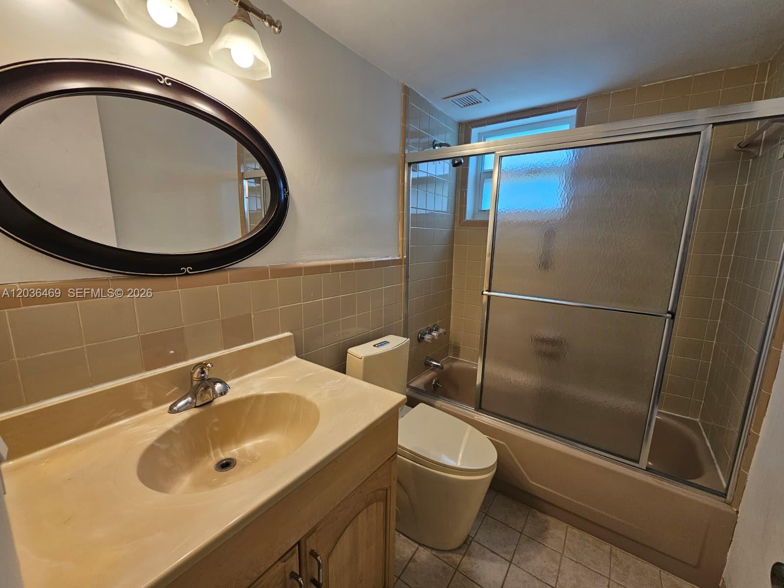 A bathroom features a tan vanity, a toilet, and a shower-tub combo with tiled walls — 520 NE 38th St # 12, Miami FL 33137, MIAMI, FL