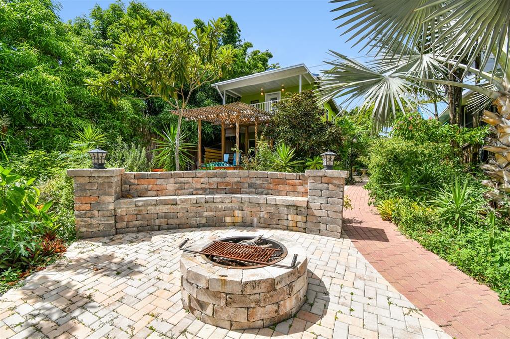 A stone fire pit and curved bench sit on a brick patio in a lush garden — 3203 E YUKON STREET, TAMPA, FL