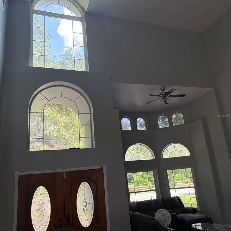 A high-ceilinged living room features multiple arched windows, a ceiling fan, and double entry doors — 1931 OAK RIDGE COURT, CLEARWATER, FL