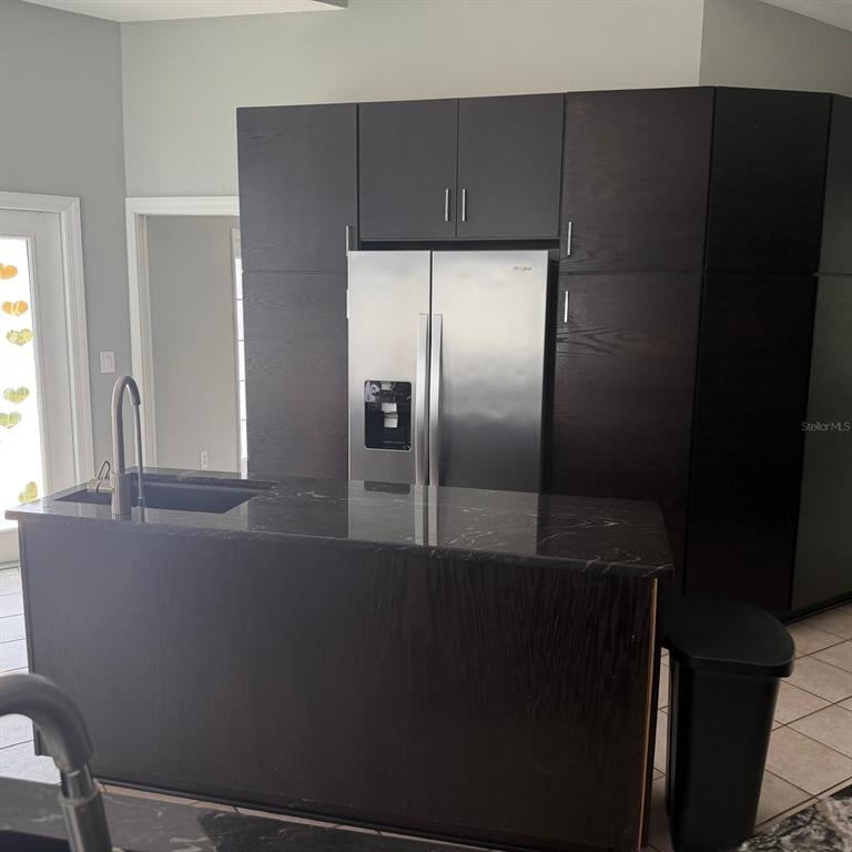 A kitchen features a dark island with a sink and dark cabinetry surrounding a refrigerator — 1931 OAK RIDGE COURT, CLEARWATER, FL