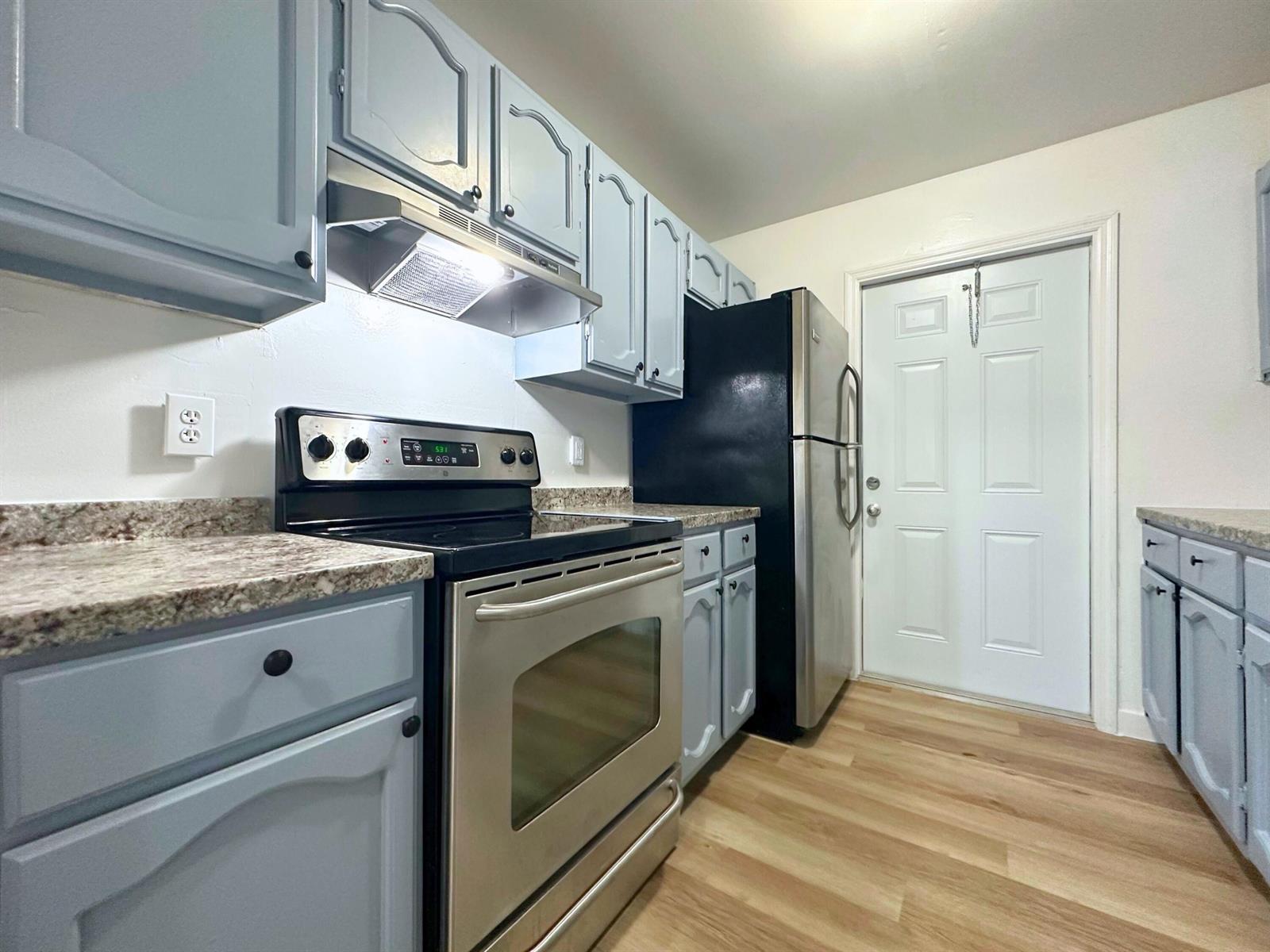 A kitchen features light blue cabinets, granite countertops, stainless steel appliances, and light wood flooring — 3662 Davis Road # 3668, Palm Springs FL 33461, PALM SPRINGS, FL