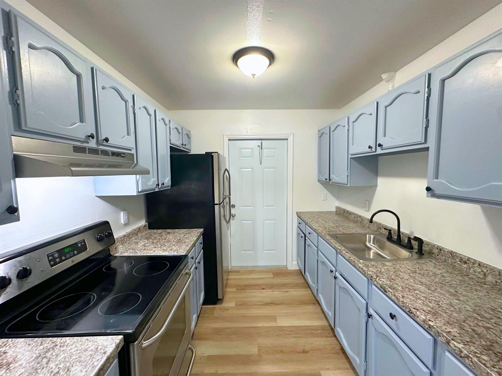 A galley kitchen features light blue cabinets, granite-look countertops, and black appliances — 3662 Davis Road # 3668, Palm Springs FL 33461, PALM SPRINGS, FL