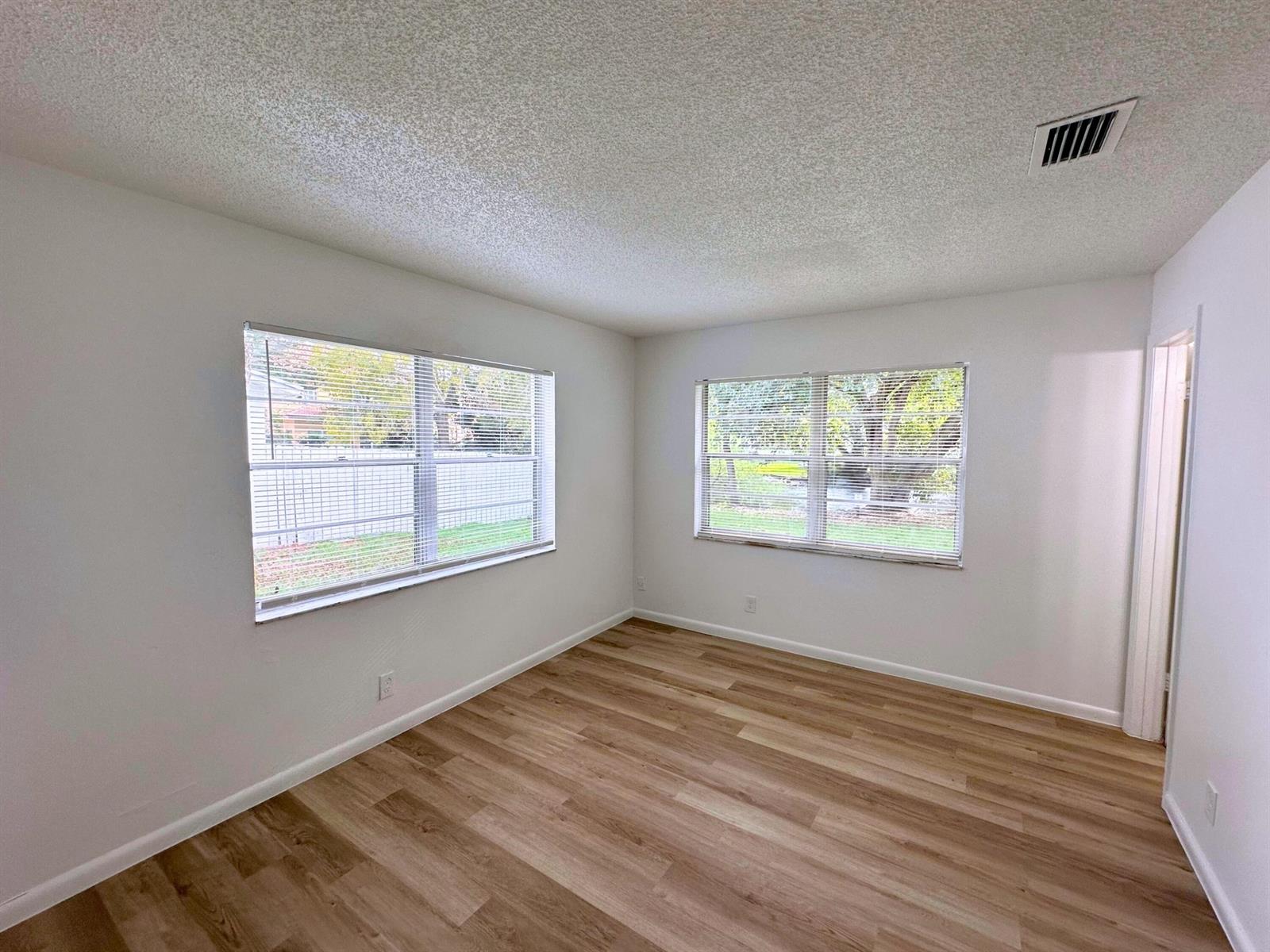 An empty bedroom features white walls, wood-look flooring, and two windows with blinds — 3662 Davis Road # 3668, Palm Springs FL 33461, PALM SPRINGS, FL