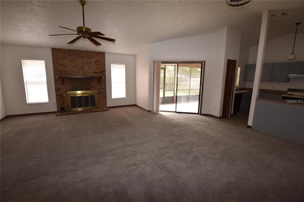 A living room features a brick fireplace, carpeted flooring, a ceiling fan, and sliding glass doors — 2585 DERBY DRIVE, DELTONA, FL