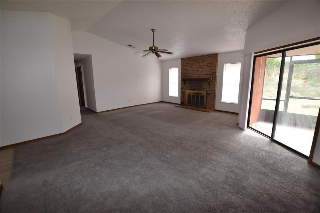 A spacious living room features gray carpeting, a brick fireplace, and sliding glass patio doors — 2585 DERBY DRIVE, DELTONA, FL