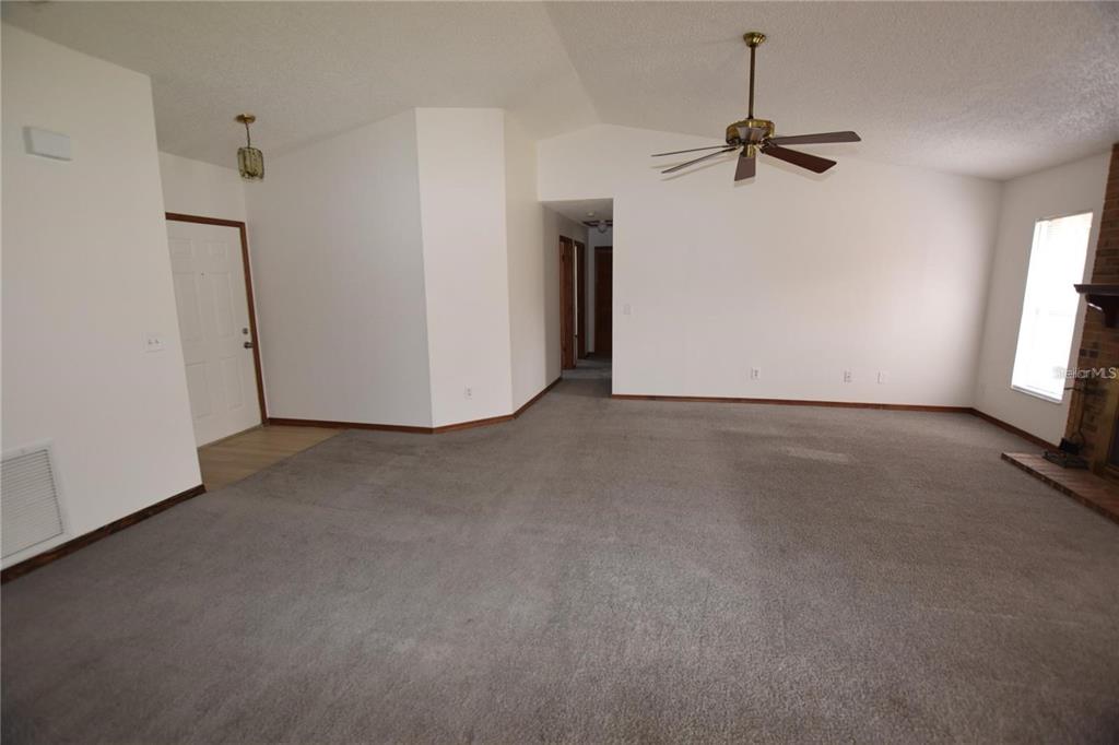 A living room with gray carpet, white walls, a ceiling fan, and a brick fireplace — 2585 DERBY DRIVE, DELTONA, FL