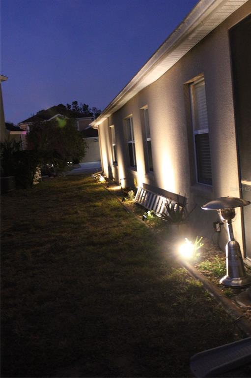 An exterior view of a house side wall illuminated by landscape lighting at dusk — 738 CORVINA DRIVE, DAVENPORT, FL