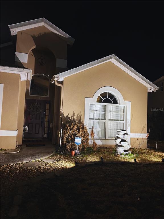 A tan stucco house exterior at night with a front entrance and a large window — 738 CORVINA DRIVE, DAVENPORT, FL