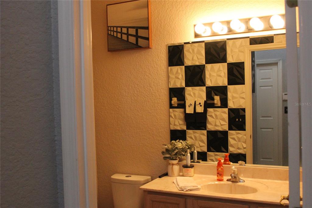 A bathroom features a checkerboard textured tile backsplash, a vanity, and a wall-mounted light fixture — 738 CORVINA DRIVE, DAVENPORT, FL