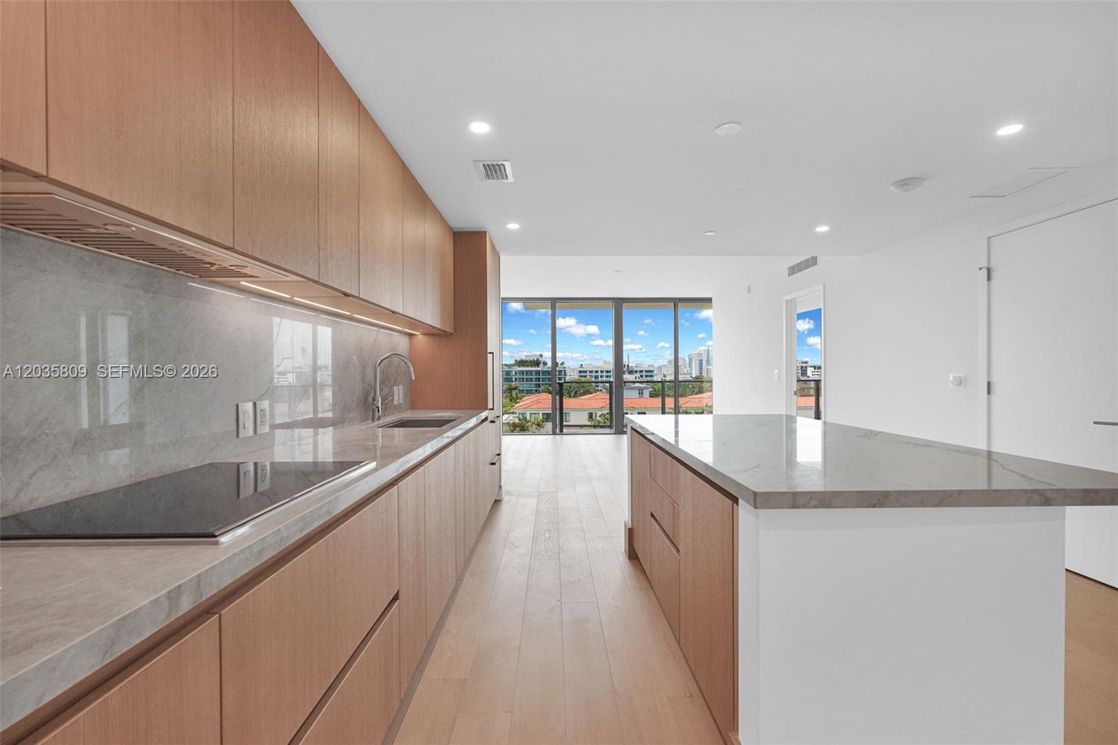 A modern kitchen features light wood cabinetry, stone countertops, and a large central island — 1176 97th st # 707, Bay Harbor Islands FL 33154, BAY HARBOR ISLANDS, FL