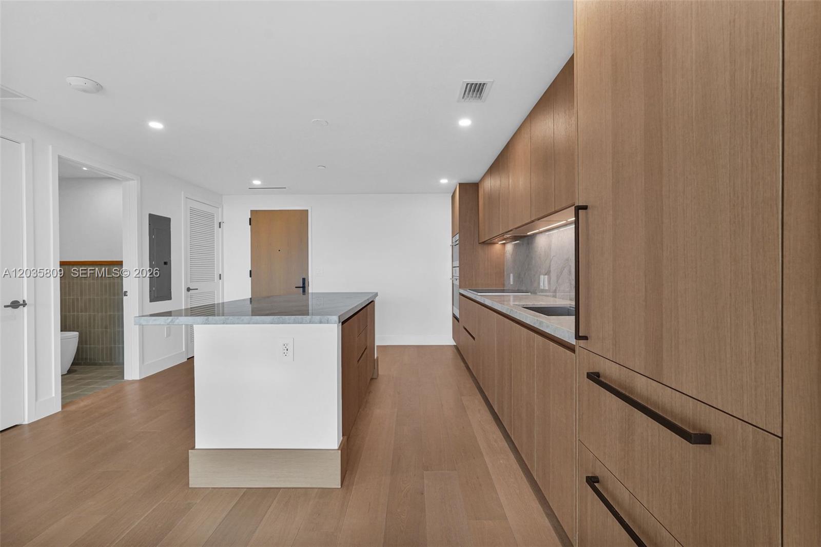 A modern kitchen features wood-toned cabinetry, a marble-topped island, and light hardwood flooring — 1176 97th st # 707, Bay Harbor Islands FL 33154, BAY HARBOR ISLANDS, FL