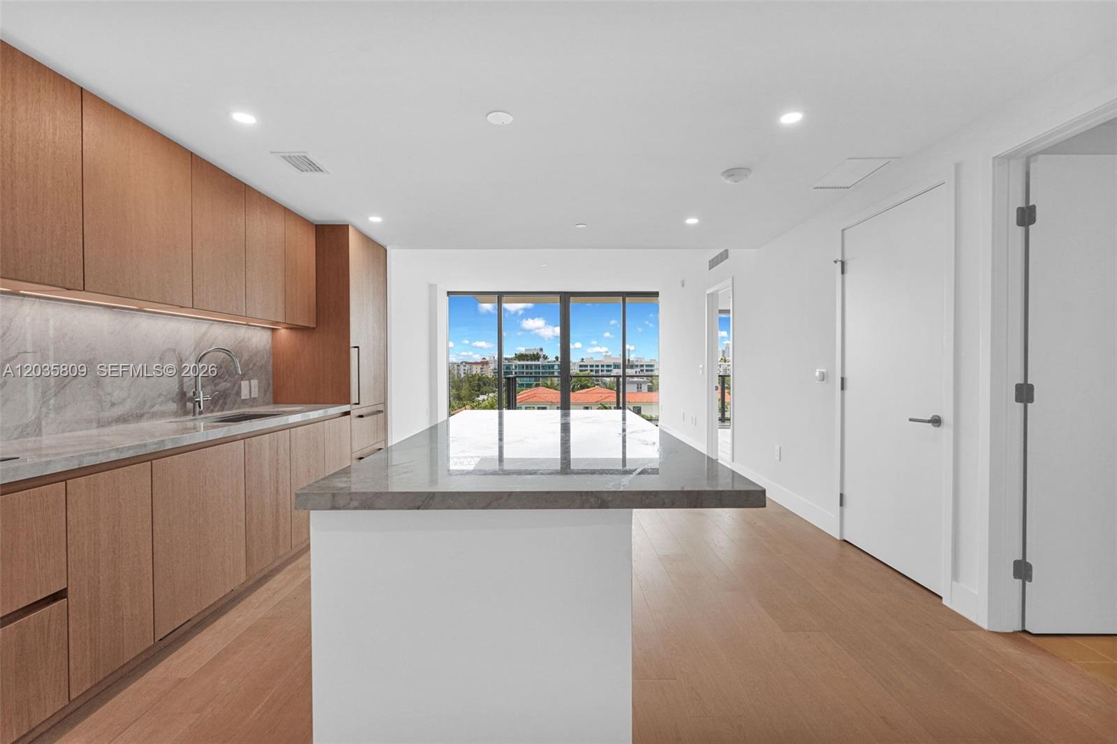 A modern kitchen features wood cabinetry, a marble-topped island, and a view of the outdoors — 1176 97th st # 707, Bay Harbor Islands FL 33154, BAY HARBOR ISLANDS, FL