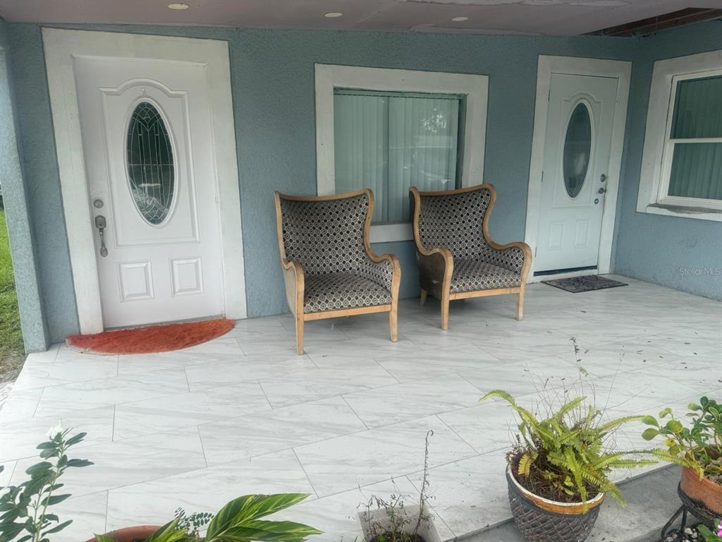 A covered porch features two patterned armchairs, two white doors, and light-colored tiled flooring — 1509 NEIL STREET, PLANT CITY, FL