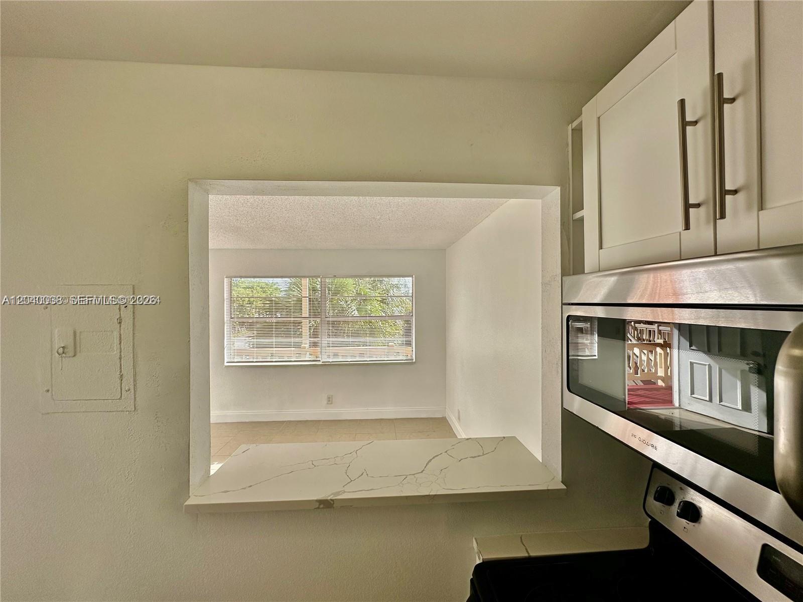 A kitchen pass-through window overlooks a bright room with tile flooring and a window — 241 SE 9th Ave # 207, Pompano Beach FL 33060, POMPANO BEACH, FL