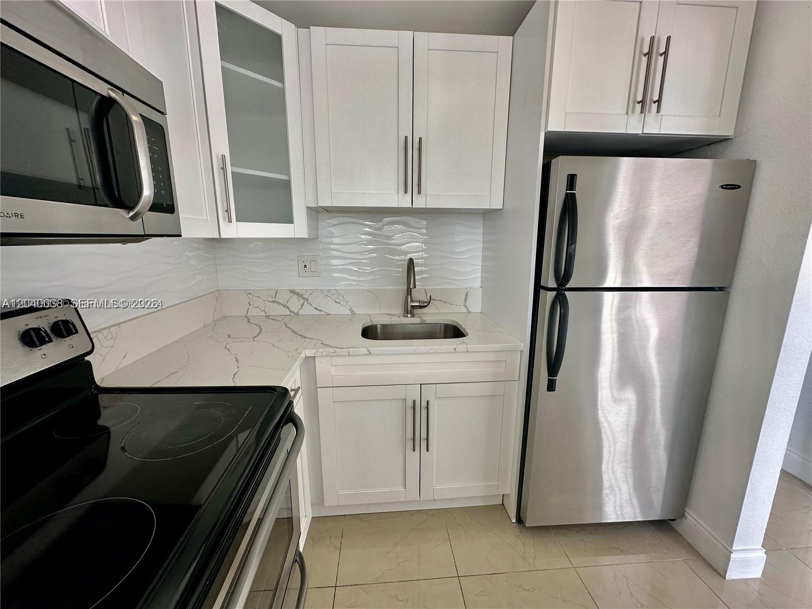 A kitchen features white cabinets, stainless steel appliances, and a marble-patterned countertop — 241 SE 9th Ave # 207, Pompano Beach FL 33060, POMPANO BEACH, FL