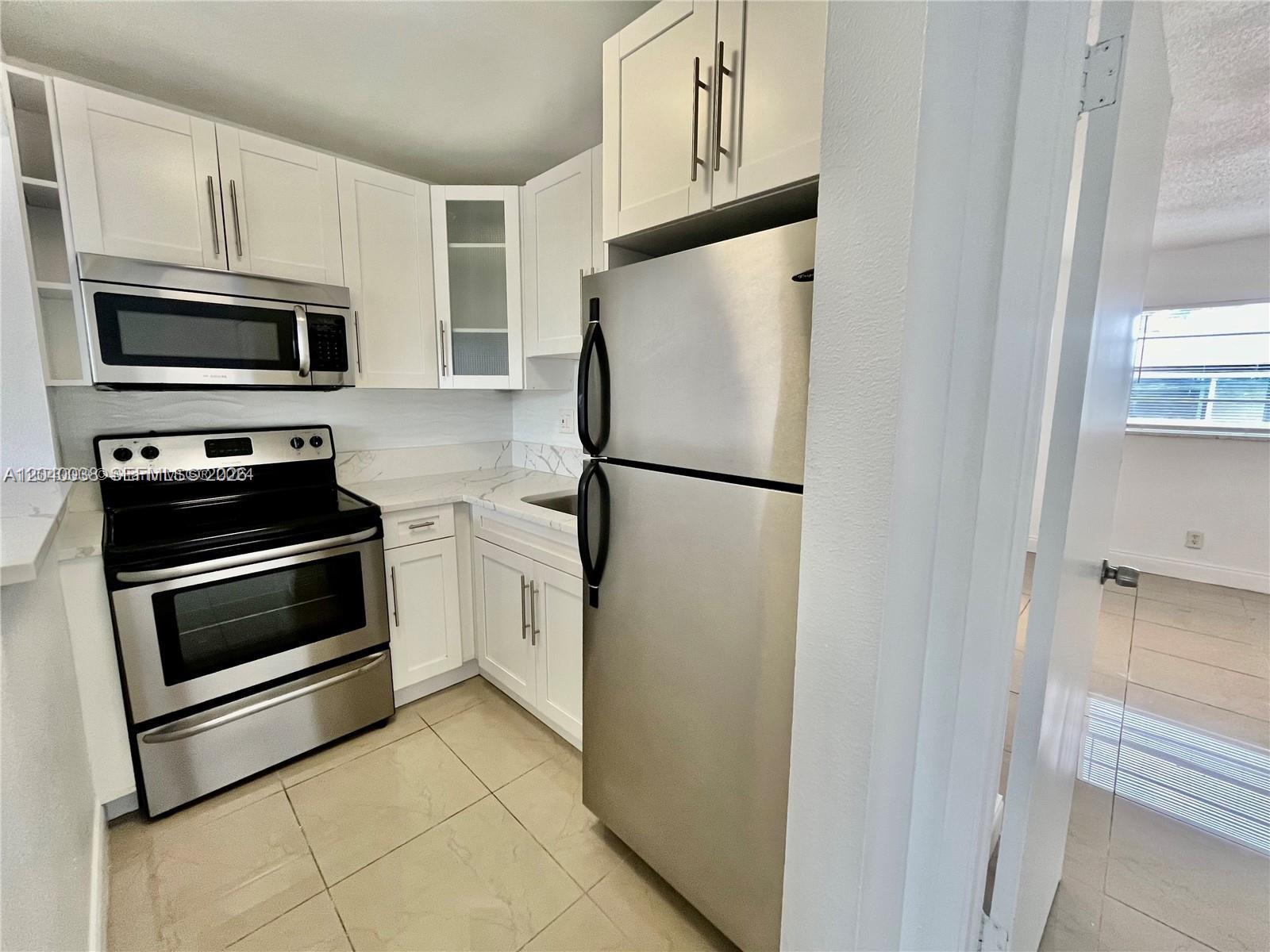 A kitchen features white cabinets, stainless steel appliances, and light-colored tile flooring — 241 SE 9th Ave # 207, Pompano Beach FL 33060, POMPANO BEACH, FL