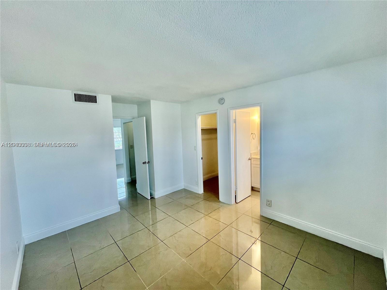 A room with light-colored tile flooring, white walls, and two doorways leading to a closet and bathroom — 241 SE 9th Ave # 207, Pompano Beach FL 33060, POMPANO BEACH, FL