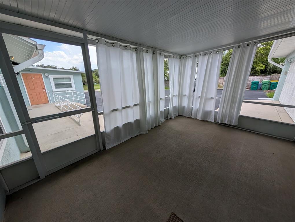 A carpeted enclosed porch features white curtains, screen walls, and a view of a neighboring building — 321 W PENNSYLVANIA AVENUE, DELAND, FL