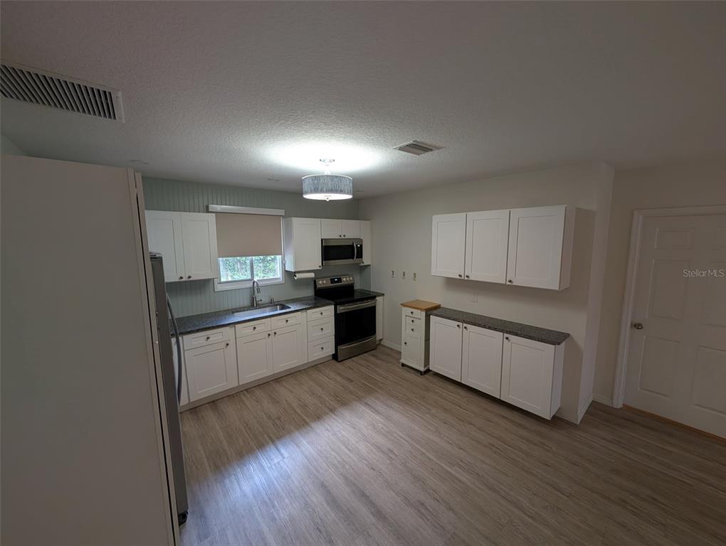 A kitchen features white cabinets, dark countertops, stainless steel appliances, and light wood-look flooring — 321 W PENNSYLVANIA AVENUE, DELAND, FL