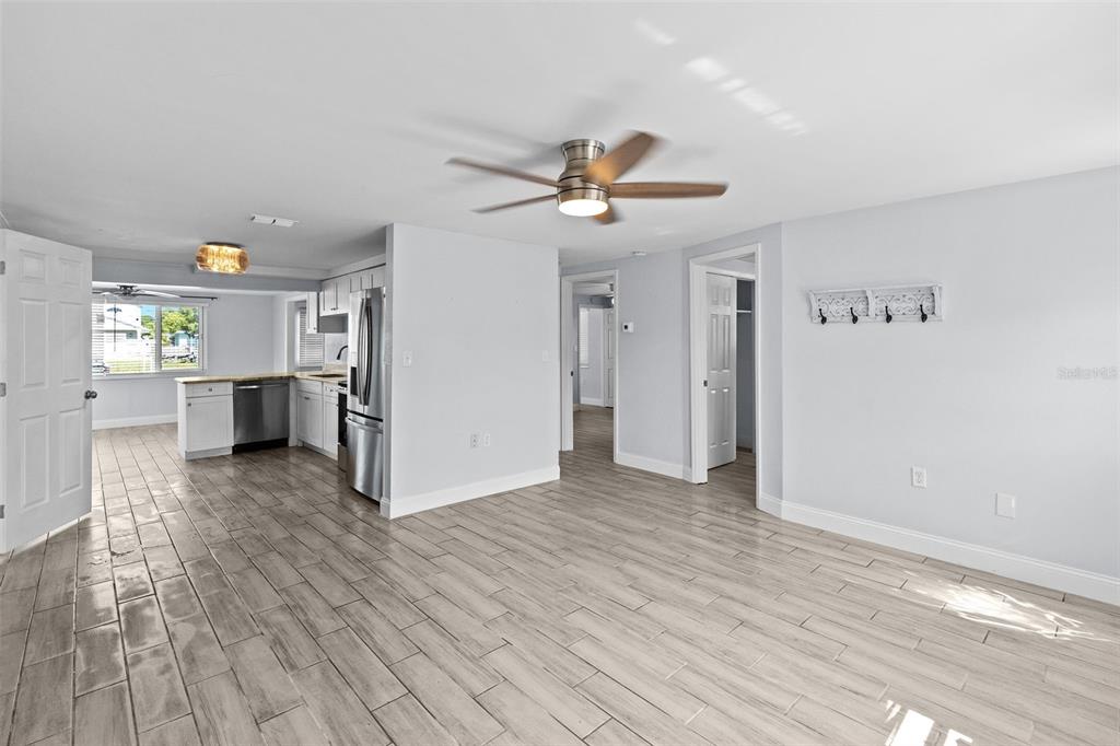 An open-concept living area with light wood-look tile flooring, a ceiling fan, and a kitchen — 13916 SOMMERS AVENUE, HUDSON, FL