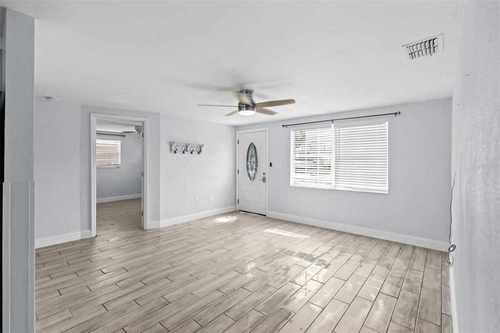 A living room with light gray walls, wood-look tile flooring, a ceiling fan, and a front door — 13916 SOMMERS AVENUE, HUDSON, FL