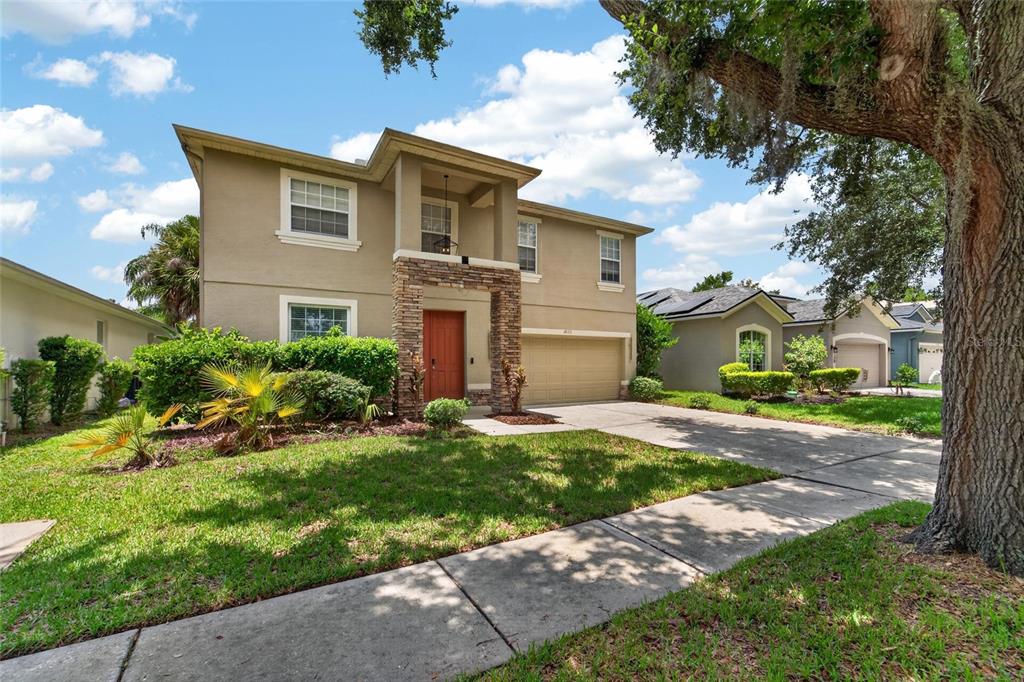 A two-story suburban house with a tan stucco exterior, stone accents, and a concrete driveway — 19128 MEADOW PINE DRIVE, TAMPA, FL