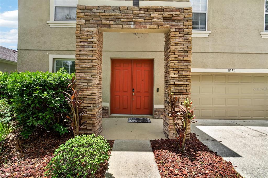 A stone-accented entryway features double red doors and a concrete walkway leading to the home — 19128 MEADOW PINE DRIVE, TAMPA, FL